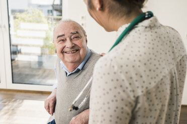Älterer Mann lächelt Krankenschwester zu Hause an - UUF12868