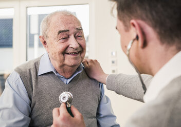 Älterer Mann lächelt Krankenschwester mit Stethoskop zu Hause an - UUF12877