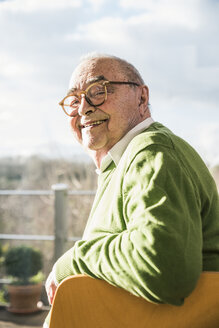Porträt eines lächelnden älteren Mannes, der auf einem Stuhl am Fenster sitzt - UUF12889