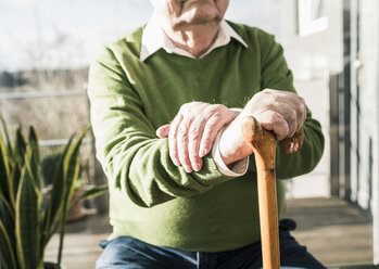 Älterer Mann sitzt am Fenster und stützt sich auf einen Stock - UUF12896