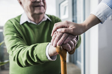 Nahaufnahme einer Frau, die die Hand eines älteren Mannes hält, der sich auf einen Gehstock stützt - UUF12897