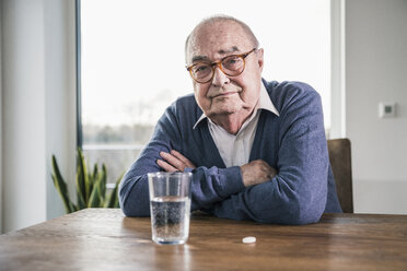 Portrait of senior man sitting at table with pill and glass of water - UUF12901