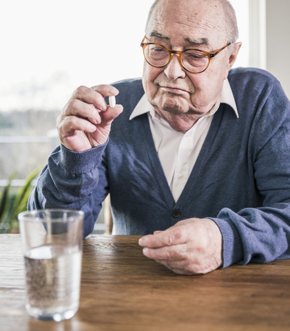 Porträt eines älteren Mannes, der mit einer Pille und einem Glas Wasser am Tisch sitzt, lizenzfreies Stockfoto