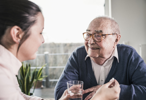 Woman holding pill and glass of water for smiling senior man stock photo