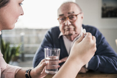 Woman holding pill and glass of water for senior man - UUF12904