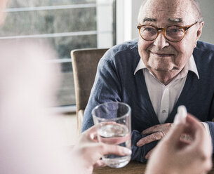 Woman holding pill and glass of water for smiling senior man - UUF12906