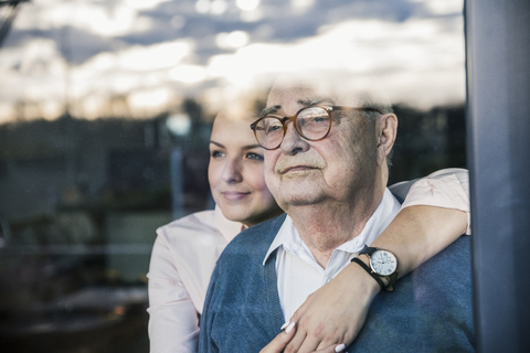 Porträt einer jungen Frau, die einen älteren Mann am Fenster umarmt, lizenzfreies Stockfoto