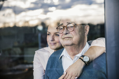 Portrait of young woman embracing senior man at the window - UUF12908