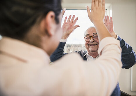 Glücklicher älterer Mann mit erhobenen Händen, der eine junge Frau ansieht - UUF12912
