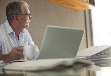 Geschäftsmann trinkt eine Tasse Kaffee am Laptop - CAIF02948