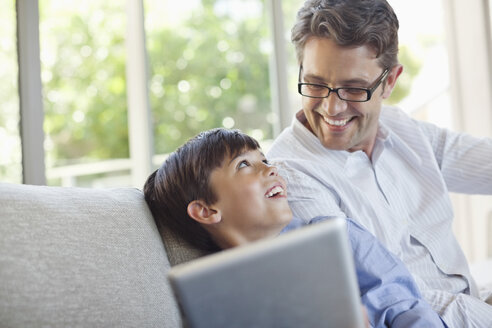 Vater und Sohn benutzen einen Tablet-Computer auf dem Sofa - CAIF02955