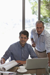 Older man and younger man working together at desk - CAIF02982