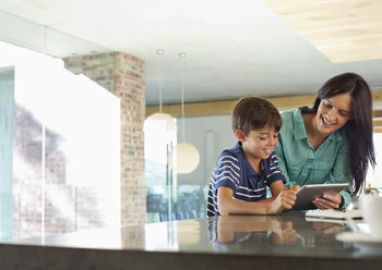 Mother and son using tablet computer in kitchen - CAIF03013