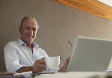 Older man having cup of coffee at desk - CAIF03016