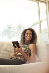 Woman using tablet computer on sofa - CAIF03054