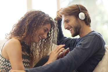 Couple listening to headphones on sofa - CAIF03059