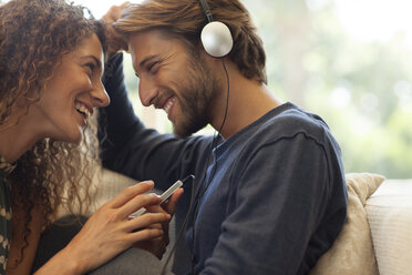 Couple listening to headphones on sofa - CAIF03063