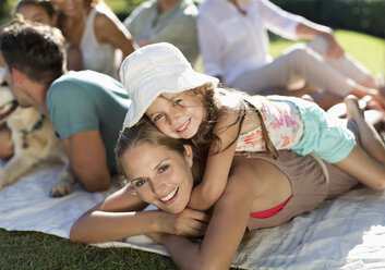 Mother and daughter relaxing in grass with family - CAIF03224