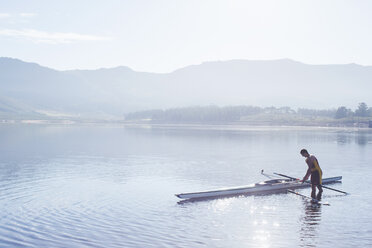 Man placing rowing scull in lake - CAIF03234