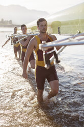 Rowing team carrying scull in lake - CAIF03248