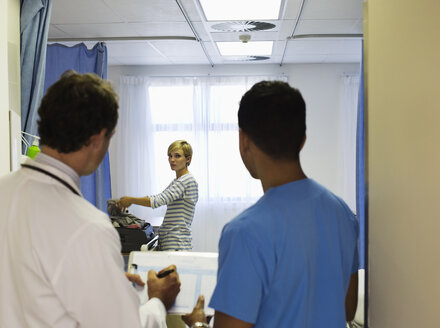 Doctor and nurse watching patient pack in hospital room - CAIF03290