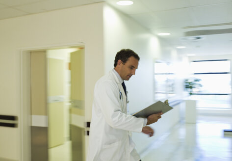 Doctor reading medical chart in hospital hallway - CAIF03291