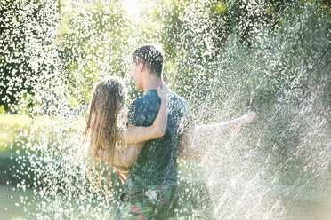 Paar spielt in Sprinkleranlage im Hinterhof - CAIF03306