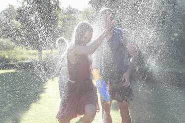 Couple playing in sprinkler in backyard - CAIF03311