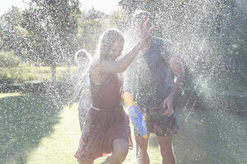 Paar spielt in Sprinkleranlage im Hinterhof - CAIF03311