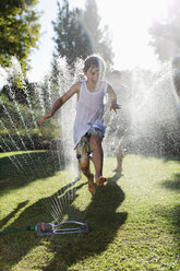 Boy playing in sprinkler in backyard - CAIF03317
