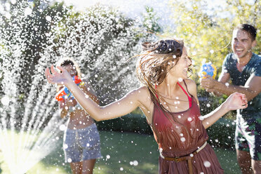 Friends playing with water guns in sprinkler - CAIF03328