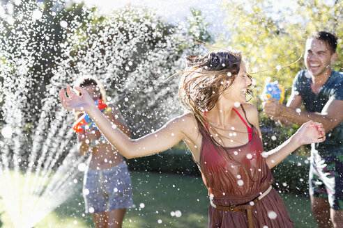 Freunde spielen mit Wasserpistolen im Rasensprenger - CAIF03328