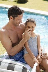 Vater trägt Sonnenschutzmittel auf die Nase seiner Tochter am Schwimmbad auf - CAIF03335