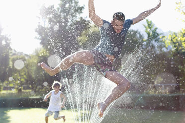 Vater und Sohn spielen im Sprinkler im Hinterhof - CAIF03338