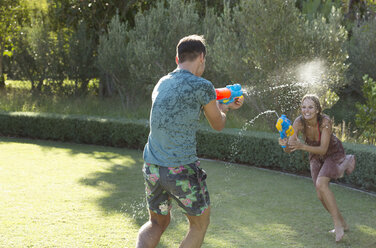 Ehepaar spielt mit Wasserpistolen im Hinterhof - CAIF03354