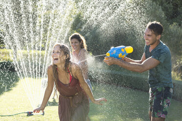 Freunde spielen mit Wasserpistolen im Sprinkler im Hinterhof - CAIF03357