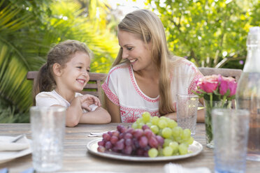 Mother and daughter smiling at table outdoors - CAIF03404