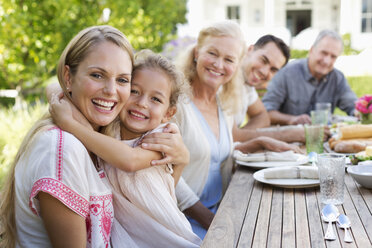 Mother and daughter hugging at table outdoors - CAIF03411