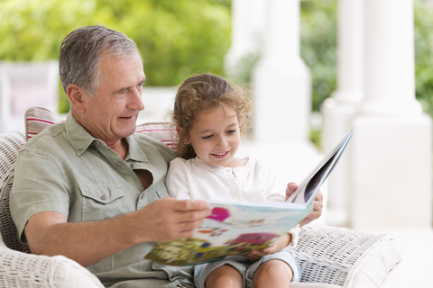 Älterer Mann liest seiner Enkelin auf der Veranda vor, lizenzfreies Stockfoto