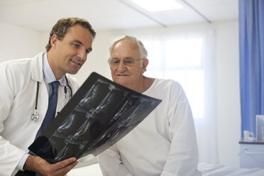 Arzt und Patient prüfen Röntgenbilder im Krankenhauszimmer - CAIF03428