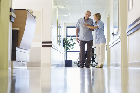 Krankenschwester hilft Patientin beim Gehen im Krankenhausflur, lizenzfreies Stockfoto