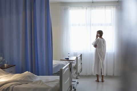 Patientin im Kittel, die im Krankenhauszimmer mit einem Handy telefoniert, lizenzfreies Stockfoto