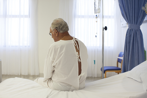 Älterer Patient trägt Kittel im Krankenhauszimmer, lizenzfreies Stockfoto