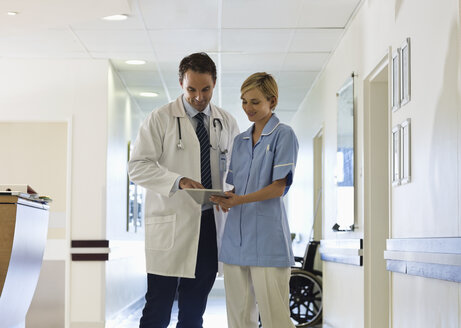 Doctor and nurse using tablet computer in hospital hallway - CAIF03446