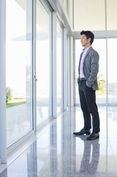 Businessman standing at office window - CAIF03504