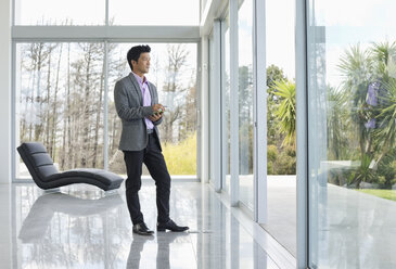 Businessman standing at office window - CAIF03505