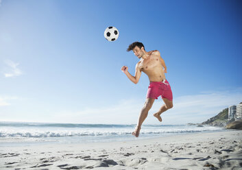 Man in swim trunks heading soccer ball on beach - CAIF03514