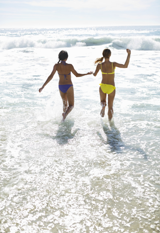 Freunde in Bikinis halten sich an den Händen und laufen ins Meer, lizenzfreies Stockfoto