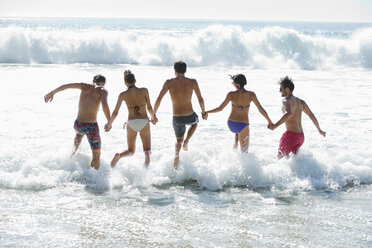 Friends holding hands and splashing in ocean - CAIF03527