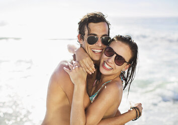 Portrait of enthusiastic couple in sunglasses hugging on beach - CAIF03531
